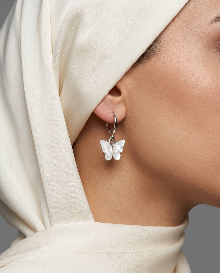 گوشواره حلقه‌ای نقره‌ای با آویز پروانه سفید صدفی روی گوش
